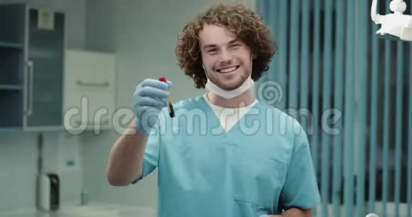 年轻的医生在镜头前戴着面具戴着蓝色的外科手套手里拿着验血盆看着视频的预览图
