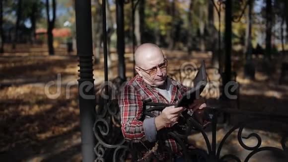 一位老人在秋天公园读一本电子书一位老年妇女收集落叶视频的预览图