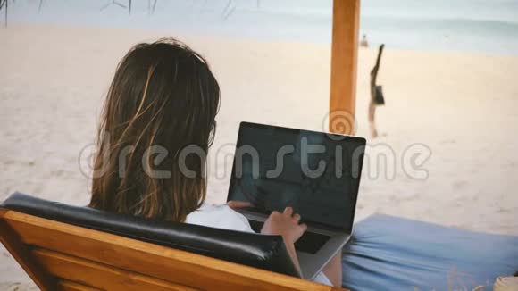 backview成功的首席执行官女商人专注于在异国海滨休闲椅上的笔记本电脑财务图表视频的预览图