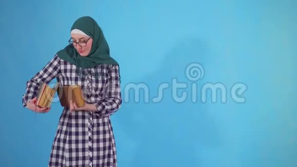 年轻的阿拉伯女学生戴着头巾带蓝色背景的书视频的预览图