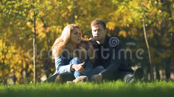 一对严肃的夫妇在秋公园坐在格子布上谈论关系视频的预览图
