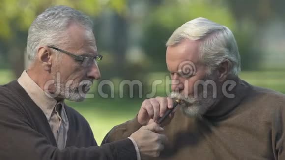 老年男性闪电雪茄给最好的朋友男人在公园的长凳上休息视频的预览图
