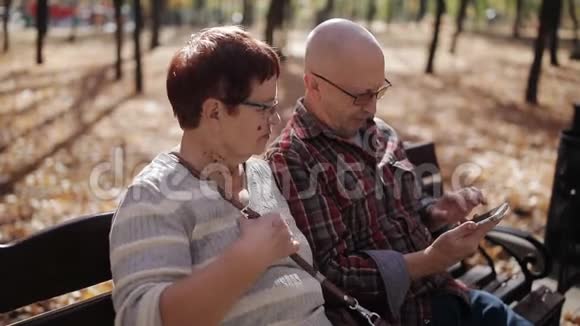 秋天公园的一对老夫妇坐在长凳上在智能手机上给自己拍照视频的预览图