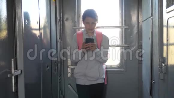 年轻的女孩旅行者的生活方式与背包站在火车的窗口与智能手机旅费视频的预览图