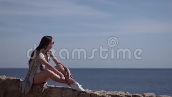 女孩坐在石栅栏上欣赏美丽的海景视频的预览图