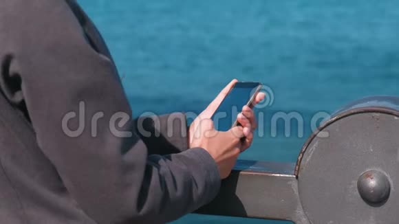 在阳光明媚秋天女人的手在站在海边的手机上键入一条信息视频的预览图