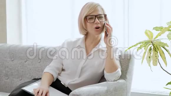 一个年轻漂亮的金发女人戴着眼镜坐在沙发上用手机说话视频的预览图