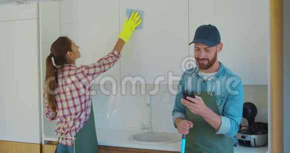 男人和女人作为一名职业清洁工穿着制服在厨房休息时和电话站在一起视频的预览图
