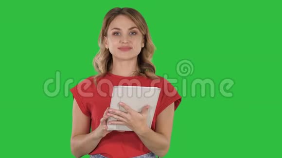 主持人女士穿着红色T恤拿着平板电脑翻页在绿色屏幕上与相机交谈Chroma键视频的预览图
