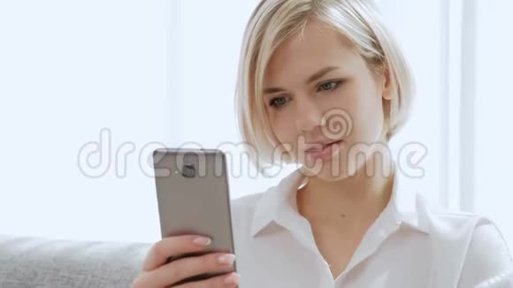一个年轻漂亮的金发女人戴着眼镜坐在沙发上用手机说话视频的预览图