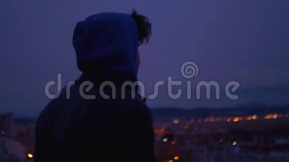晚上带着兜帽的年轻人从山上看城市慢动作4k视频的预览图