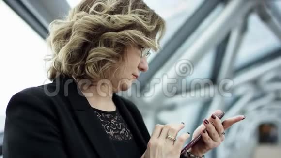 前台看到一个商务女性站着检查智能手机的内容然后停止她正在滚动监视器视频的预览图
