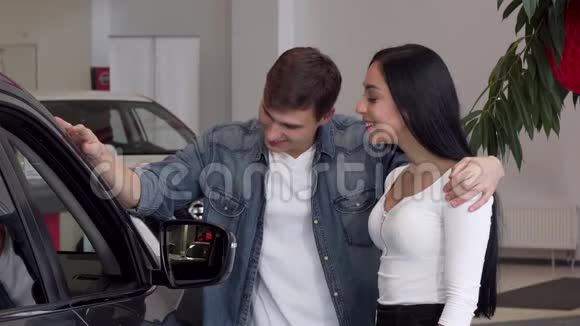 年轻夫妇在汽车经销店里挑选新车看着车里视频的预览图