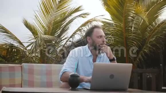 成功的年轻创意工作者用笔记本电脑在异国海滩的棕榈树下在线工作视频的预览图