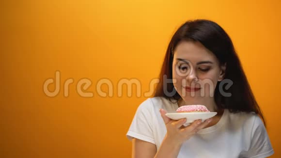 快乐的女孩闻着甜甜圈对着镜头甜食肥胖的风险视频的预览图