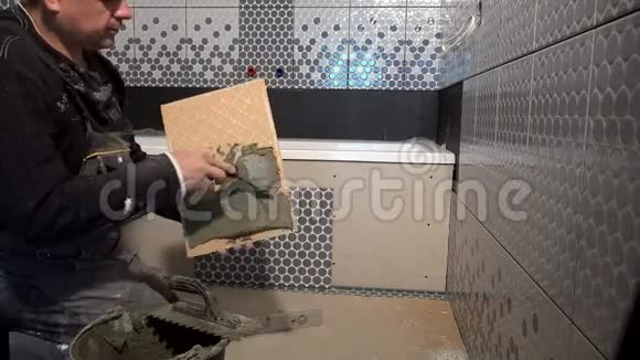 男性杂工用铲子将胶水涂在瓷砖背面视频的预览图