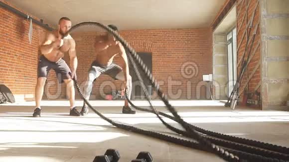 两个多民族的裸胸运动员在健身房用战绳锻炼慢动作视频的预览图