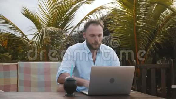 中镜头集中成功的中年商人使用笔记本电脑移动办公室在异国棕榈树海滩度假村视频的预览图