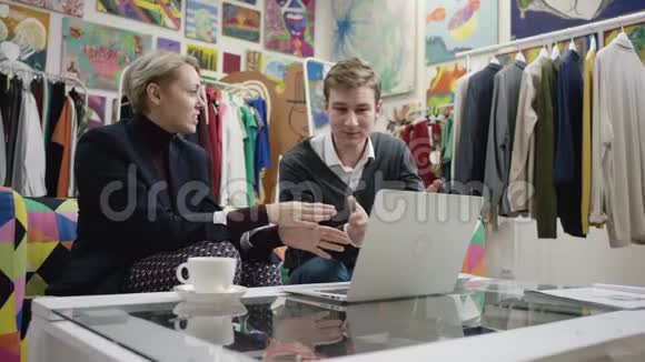成年女商人和她的年轻男雇员使用笔记本电脑讨论商业项目视频的预览图