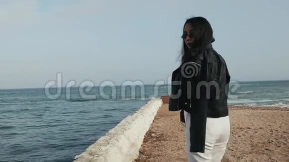 穿着皮夹克太阳镜的女孩走在大海的背景下视频的预览图
