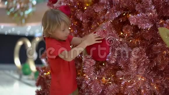 一个小男孩慢镜头把红色的圣诞装饰挂在红色和金色的圣诞树上视频的预览图