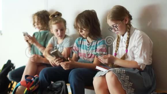 学校的孩子们拿着智能手机坐在学校的长凳上网络成瘾孩子和小玩意回到学校视频的预览图