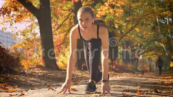 年轻的白种人女孩穿着连衣裙在起跑线上准备在秋季公园跑步视频的预览图