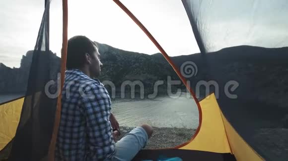 一个年轻人躺在野营帐篷里在智能手机上拍照拍摄一幅美丽的风景视频的预览图