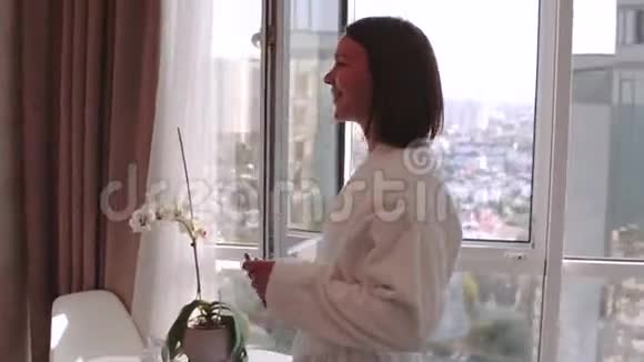 漂亮的黑发女人穿着白色浴袍享受她的新公寓度假在遥远的地方跳舞唱歌视频的预览图