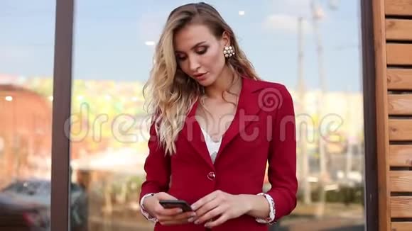 时尚的金发碧眼穿着红色智能套装使用手机和短信视频的预览图