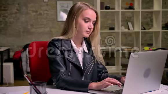 一位漂亮的白种人金发女性正在用她的笔记本电脑键盘绑着她坐在电脑旁轻松地听着音乐视频的预览图