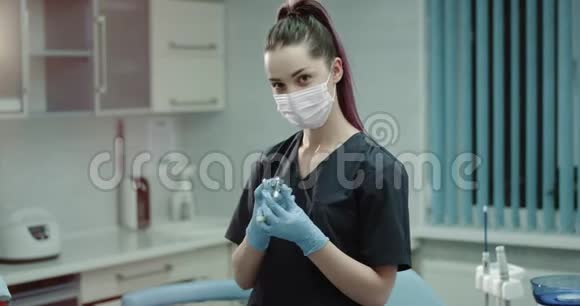 现代诊所的年轻护士助理脸上戴着外科口罩直视着摄像机手里拿着一个视频的预览图