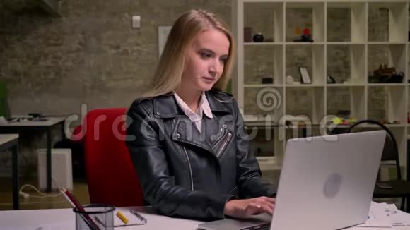 可爱的白种人金发女性正笑着轻松地看着电脑屏幕在键盘上打字挂着视频的预览图