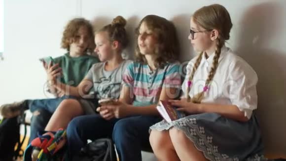 孩子们坐在学校走廊的长凳上两个同学互相展示一部智能手机学校友谊视频的预览图