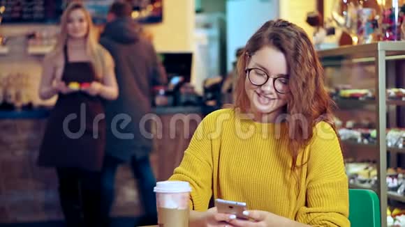 戴眼镜的漂亮女孩坐在咖啡店的桌子旁视频的预览图