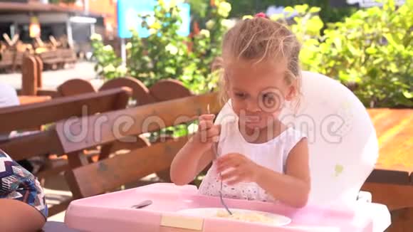 可爱的小白种人女孩在餐桌上吃意大利面坐在儿童座椅户外餐厅视频的预览图