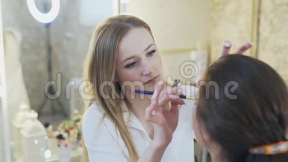 化妆专家用刷子给病人上眼睑遮瑕膏一位美丽的年轻黑发女郎的特写视频的预览图