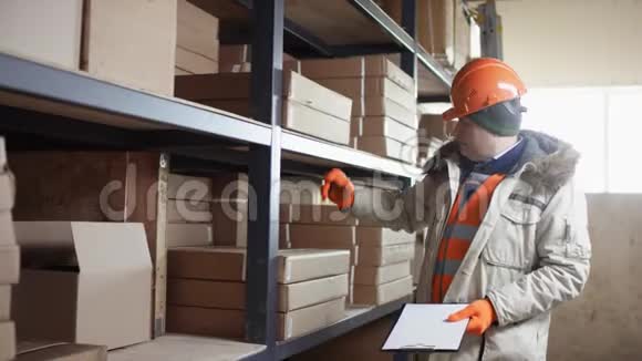 工人戴着头盔穿着工作服站在架子旁边用流动摄像机记录库存视频的预览图