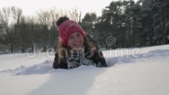 快乐微笑的女人看着镜头她躺在冬天的雪地上视频的预览图