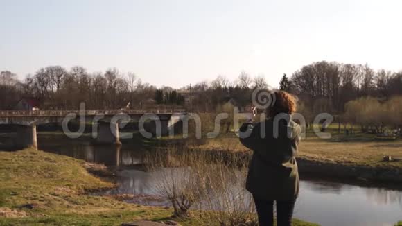 年轻女子在波罗的海国家城市萨比莱的背景下用她的手机应用程序河流拍照视频的预览图