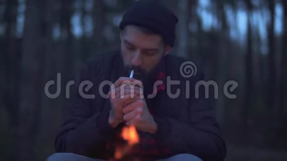 坐在森林里炉火旁的大胡子开始抽烟无胡子的家伙在森林里的火边休息视频的预览图