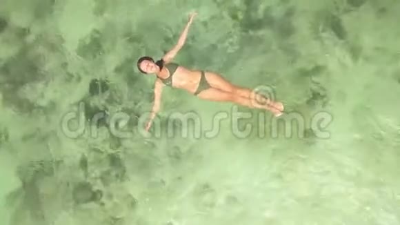 年轻女子在晶莹清澈的海水中游泳从飞行无人机俯瞰空中观光旅游妇女可在视频的预览图