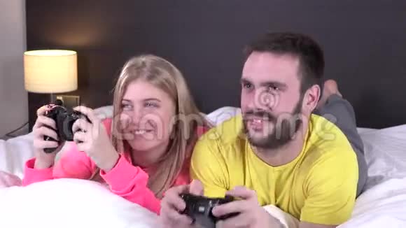 快乐的年轻夫妇在床上玩电子游戏视频的预览图
