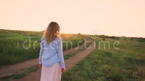 美丽的风景绿色的田野明亮的天空纤细的金发女孩在漫长的松散的道路上行走视频的预览图
