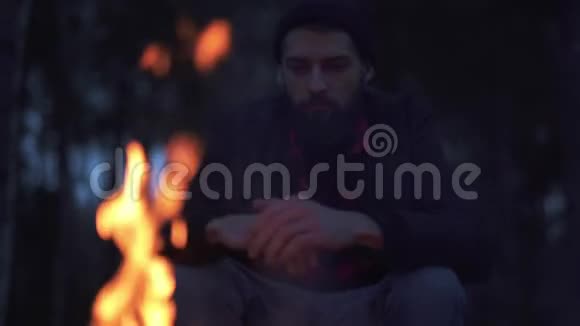 坐在椅子上的一个长着胡子的家伙在火堆上暖手森林里火堆旁的伐木工人视频的预览图