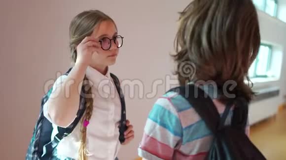 漂亮的女学生戴着眼镜两个可爱的辫子和一个背包和一个同学在学校走廊里聊天视频的预览图