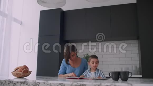 年轻的西班牙母亲和儿子坐在桌子旁一起看书微笑着视频的预览图