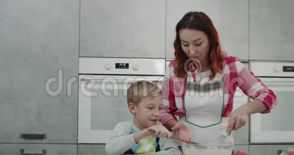 妈妈和她的儿子早上一起准备煎饼在现代厨房里吃早餐视频的预览图