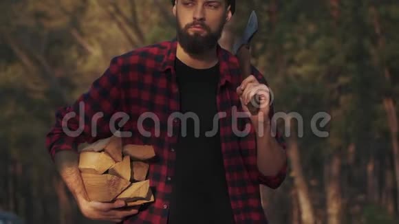 大胡子走在森林里一只手拿着砍好的木头肩上扛着斧头福斯特带着木柴慢慢视频的预览图