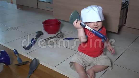 小男孩独自在厨房玩耍坐在地板上的厨师帽视频的预览图